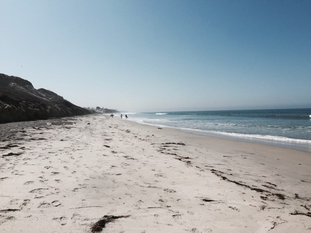 View of clifts, sand and ocean waves with people walking on the beach at South Carlsbad State Beach