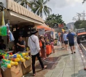 Patong Beach during Songkran, man walking down sidewalk passing stand of water guns