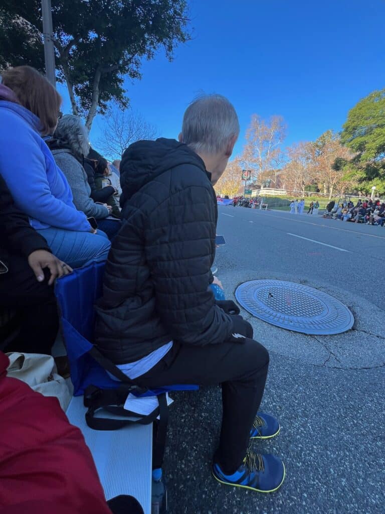 my husband sitting in his stadium seat in the grand stands watching the rose parade