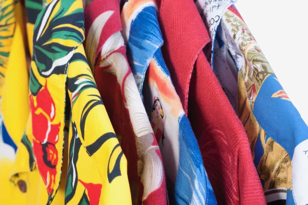 Closeup selection of five colorful yellow, red, blue and green Hawaiian shirts arranged on hangers on white background