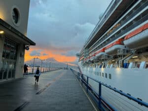 Sunset at Port of naples with Mt Vesuvius in the backgound. Cruise ship on right cruise port terminal on left with a persoon walking doen the dock toward the sunset