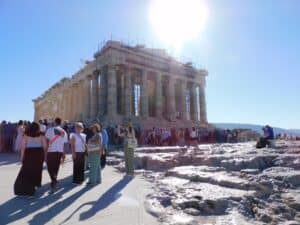 Parthenon with the sun over top and crowds of tourist in front