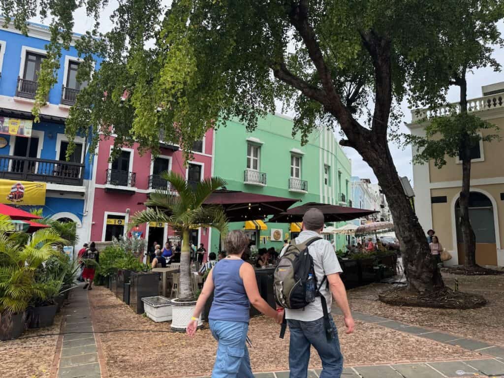 Color buildings in the background, people walking by an outdoor cafe