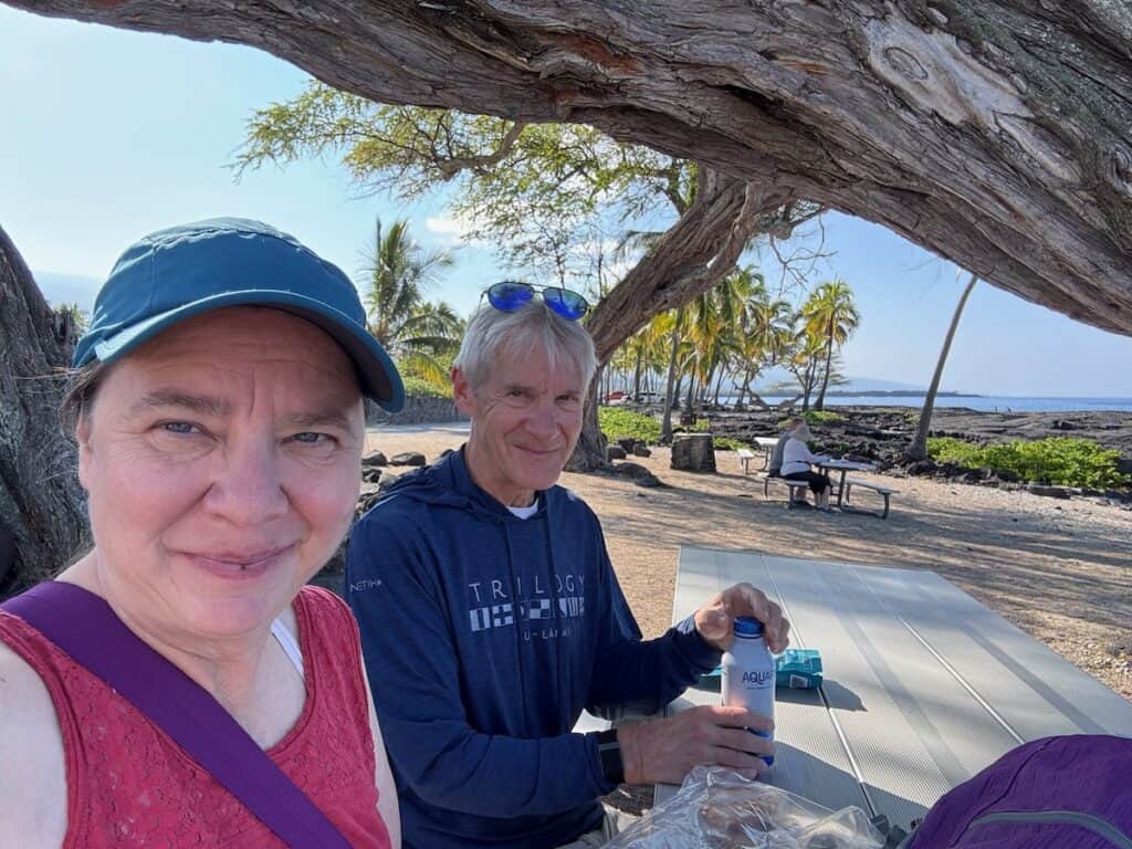 My husband and I enjoying breakfast pastries at a picnic table at Pu'uhonua O Hōnaunau National Historical Park over looking the ocean