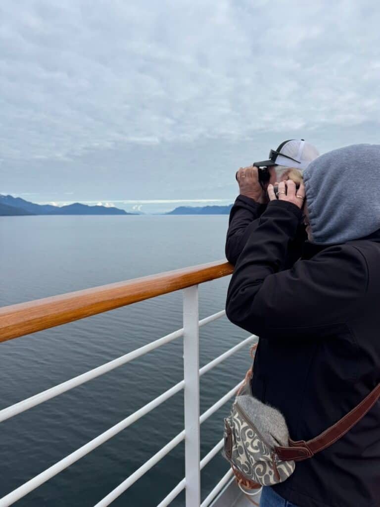 A couple using binoculars to spot whales from the deck of an Alaska Cruise